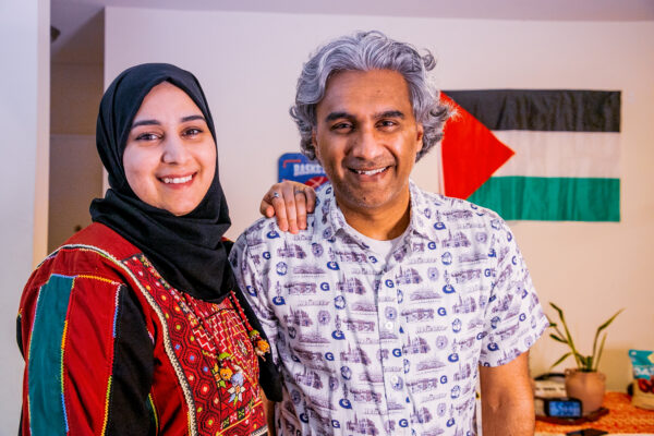 Badar stands next to his wife and smiles with the Palestinian flag in the background