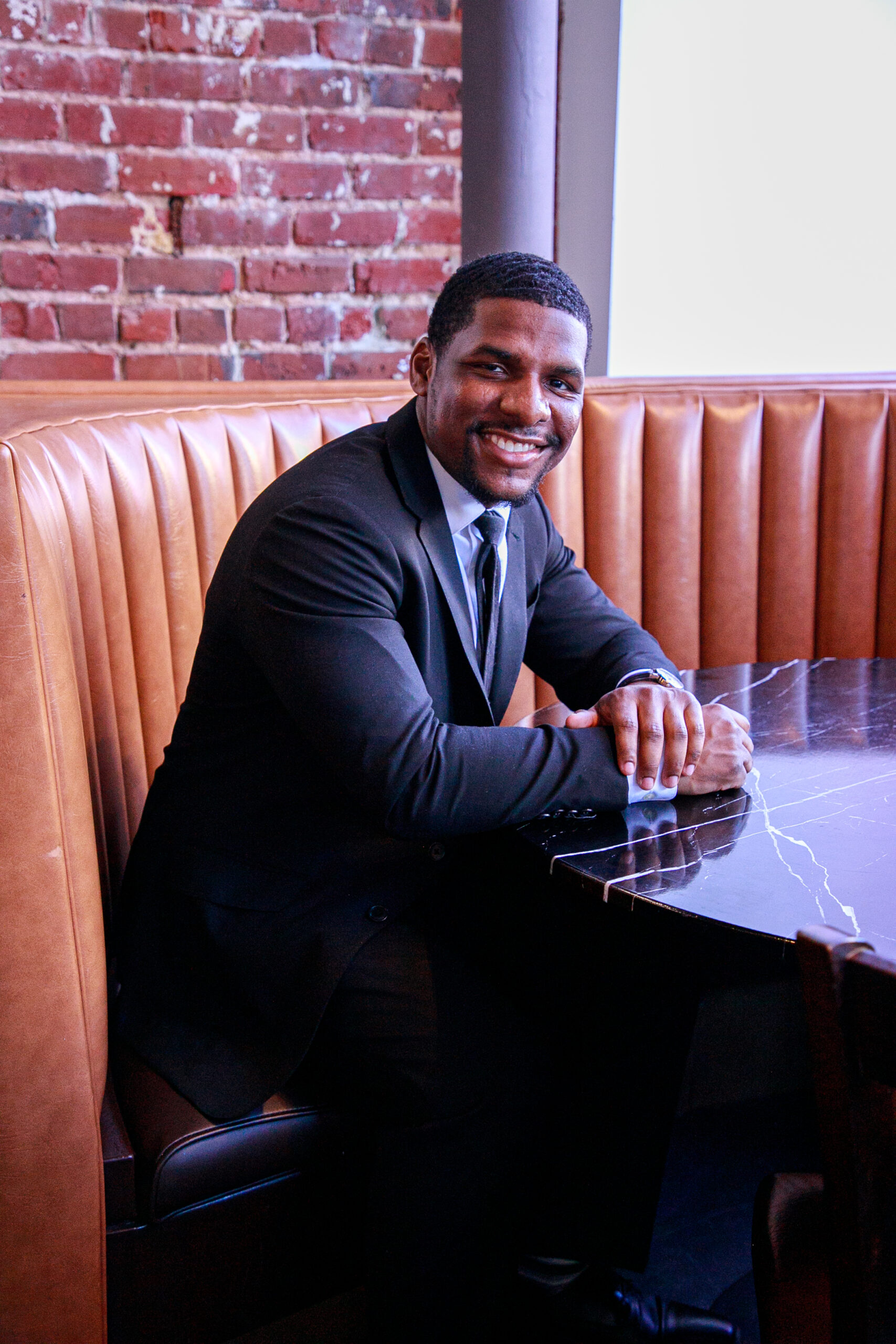 Alton Coston, a young Black man, dressed neatly in suit and smiling brightly at the camera