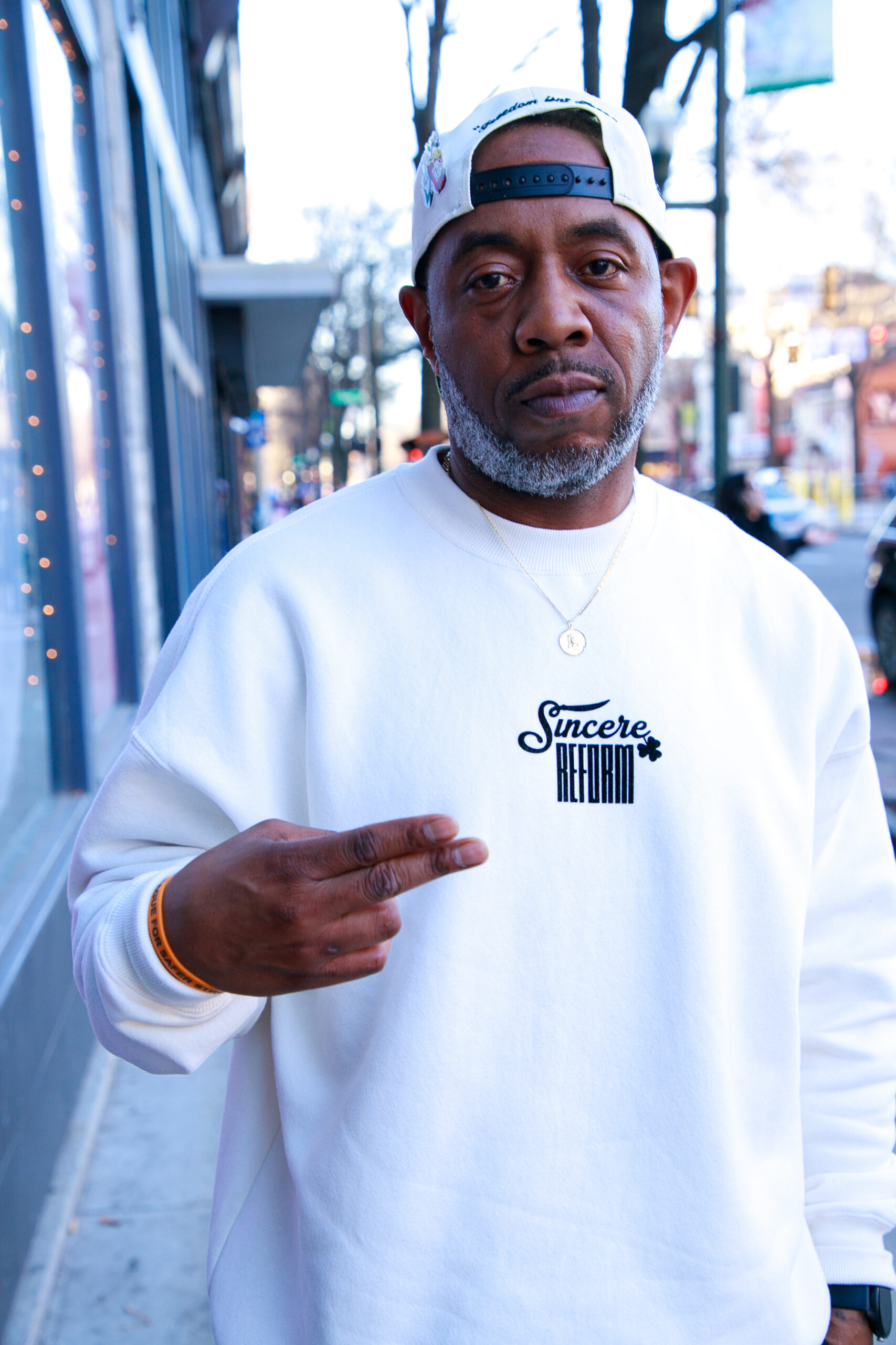 Shah, a Black man wearing a white pullover with the word "Sincere - Reform" on the front of his shirt.