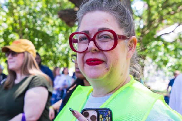 Heather, wearing bright red lipstick and matching red glasses, smiles brightly at the camera