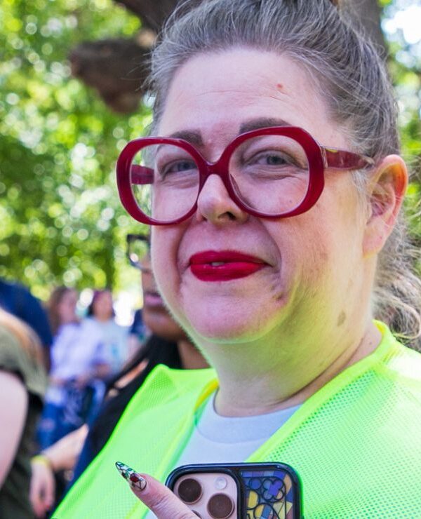 Heather, wearing bright red lipstick and matching red glasses, smiles brightly at the camera