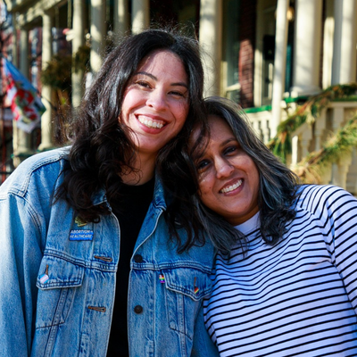 Two women smile towards a camera.