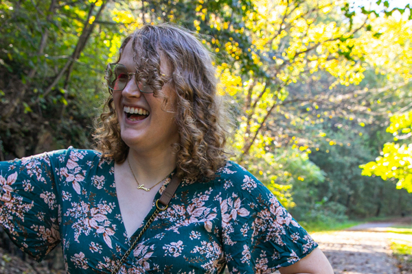 A portrait of a curly haired blonde white woman smiling towards a camera.
