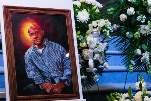 A painting of a black man is set next to a casket and bouquet of flowers.