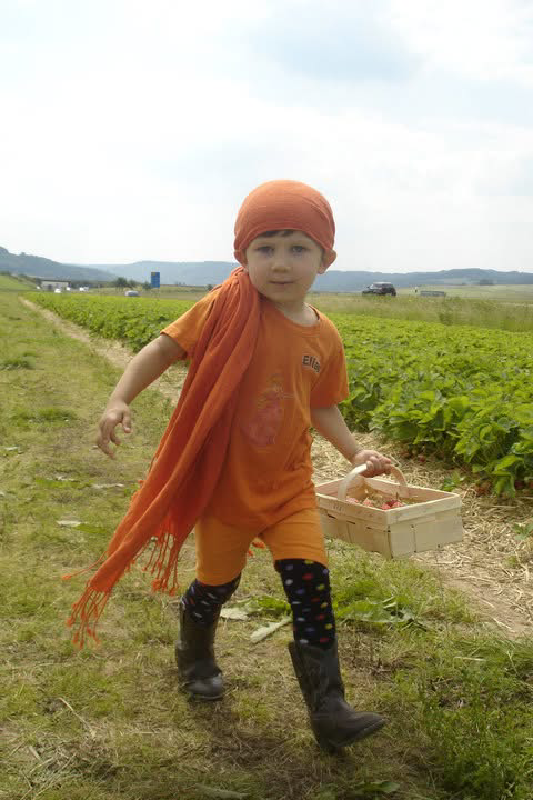 Young Eliza dressed stylishly in orange with an orange scarf draped over her should at a pumpkin patch