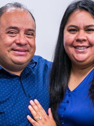 Pastor Manuel and his wife Laura, wearing matching blue, smile warmly at the camera