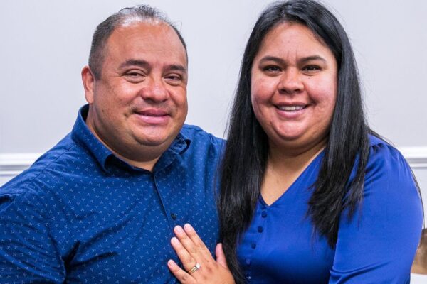 Pastor Manuel and his wife Laura, wearing matching blue, smile warmly at the camera