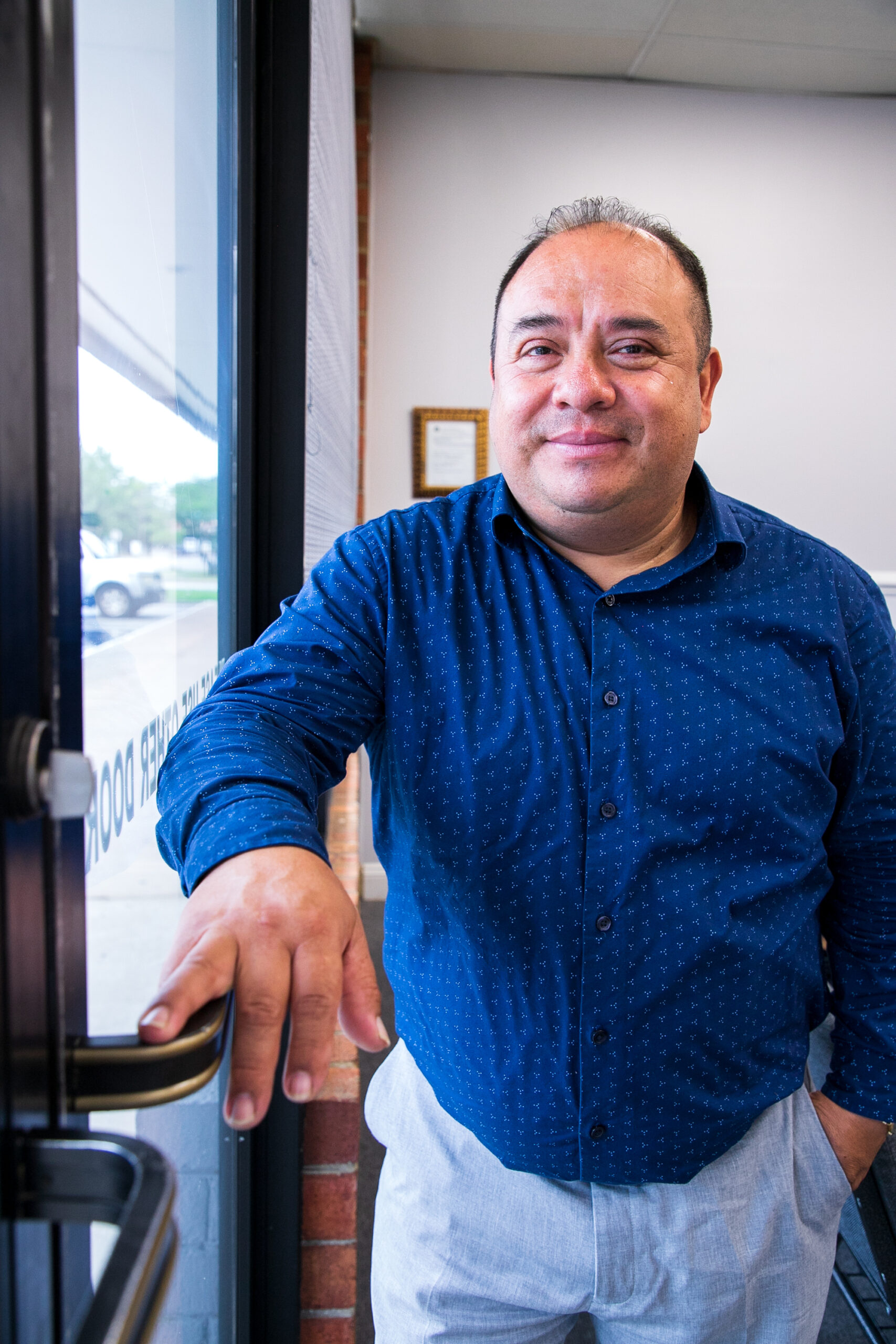 Pastor Manuel stands by his church's door and smiles warmly at the camera