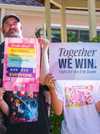 Three adults and two teenagers holding up signs to stay anonymous smiling at the camera
