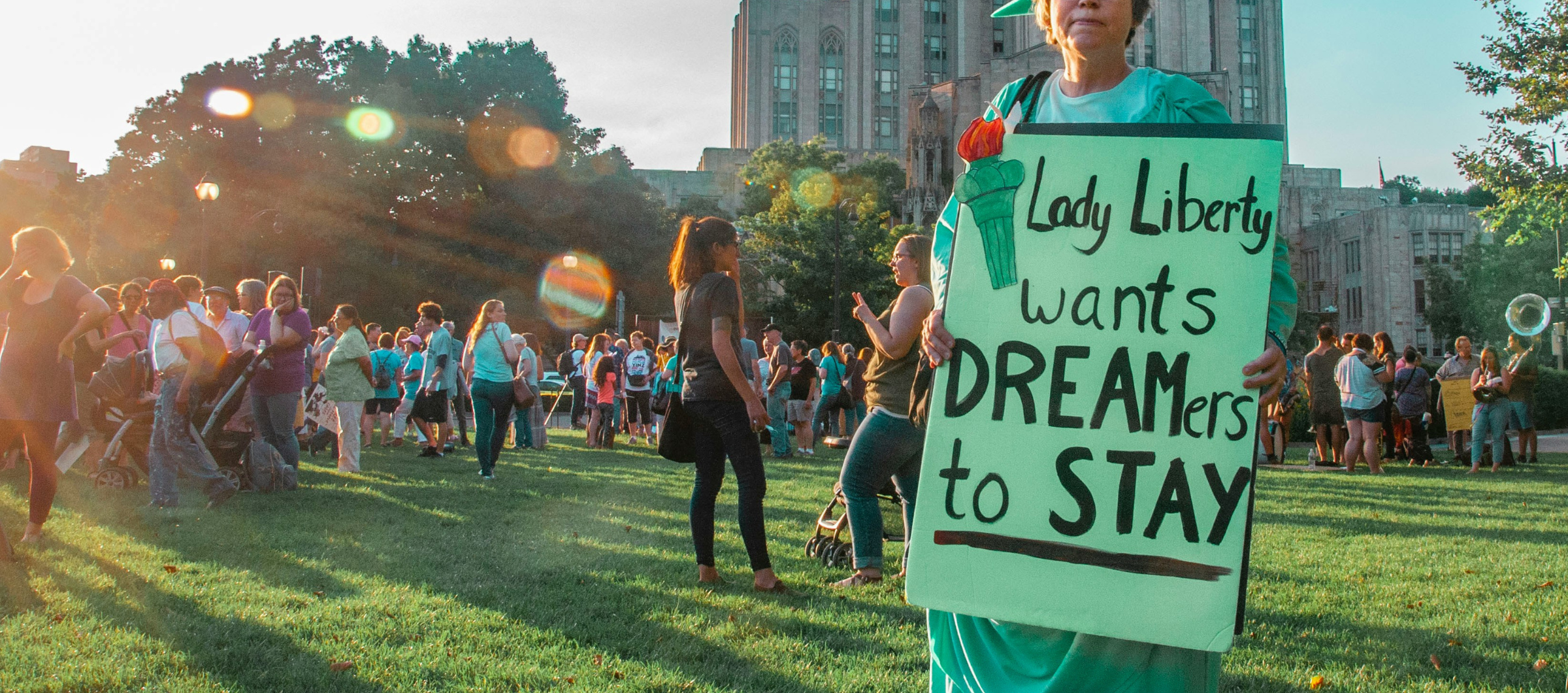 a protester dressed as Lady Liberty held a protest sign that says "Lady Liberty Wants Dreamers to Stay."