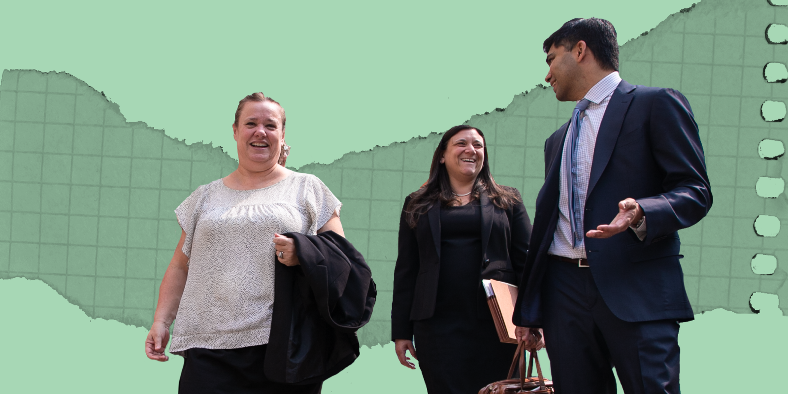 Three people in professional clothing walk together towards the same direction while in conversation.