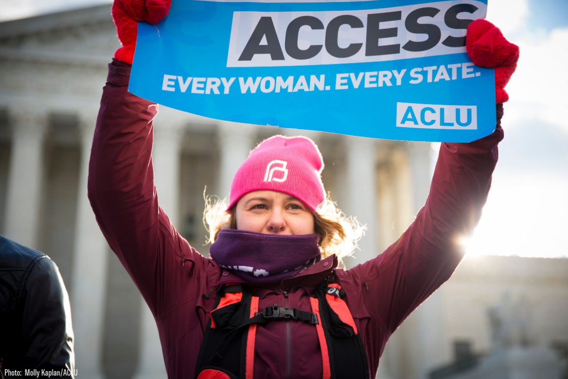 A white woman holding an ACLU branded sign that said "Abortion Access. Every Woman. Every State."
