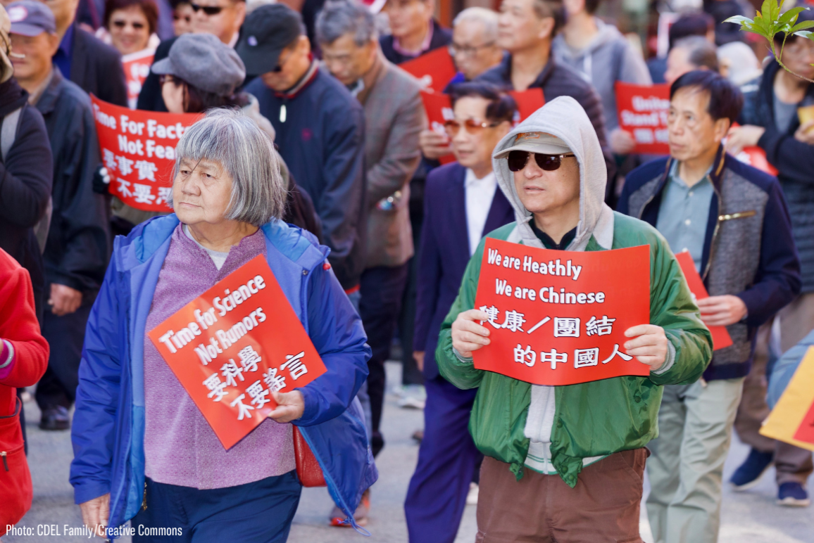 two Asian Americans holding protest signs that say "time for science, not rumors" and "we are chinese, we're healthy"