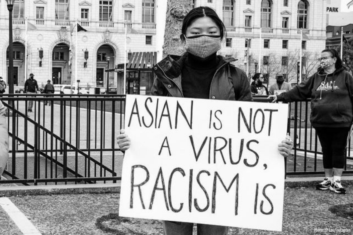 an Asian woman held a sign that says "Asian is not a virus, racism is"