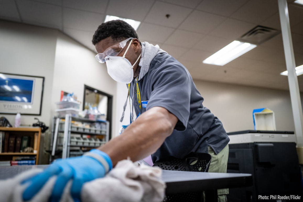 a Black man wearing a mask and cleaning a table during the COVID-19 pandemic