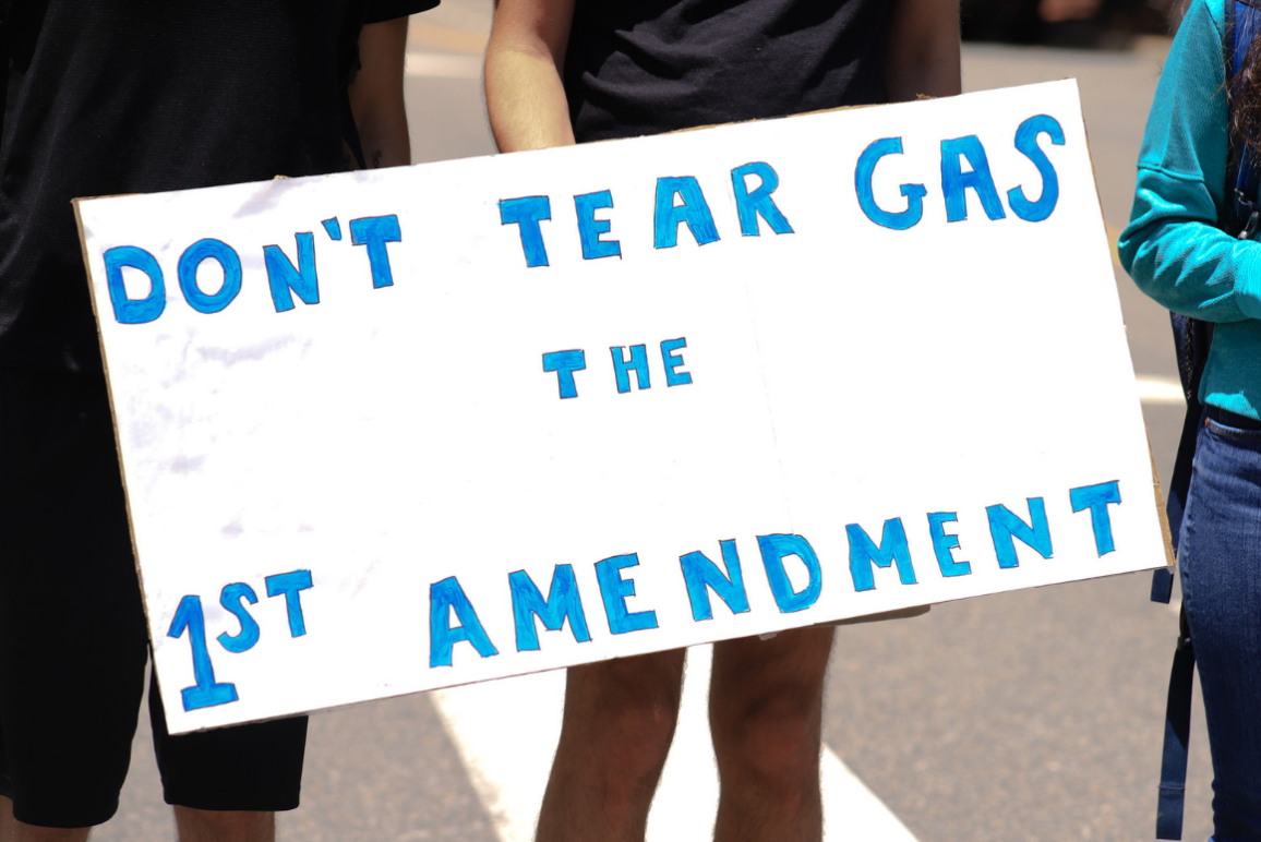 a white sign with blue text that says "don't tear gas the first amendment"