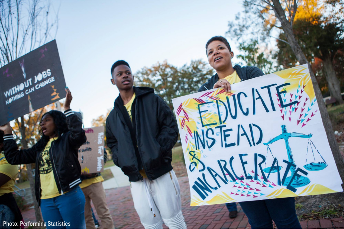 a black woman holding a sign that says "educate instead of incarcerate"