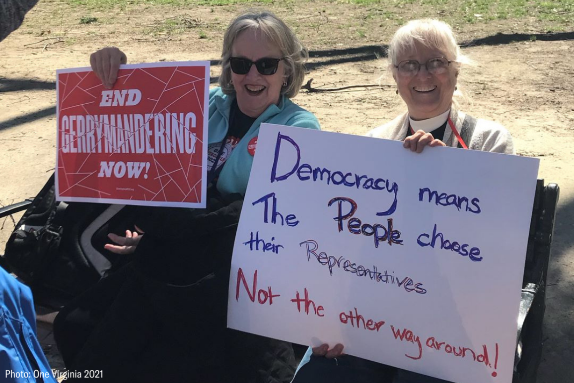 two protesters holding signs that say "End gerrymandering now" and "Democracy means the people choose their reps, not the other way around"
