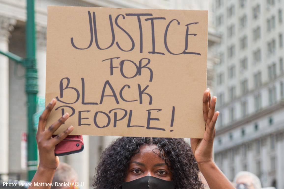 a black woman holding a cardboard sign that says "justice for black people!"