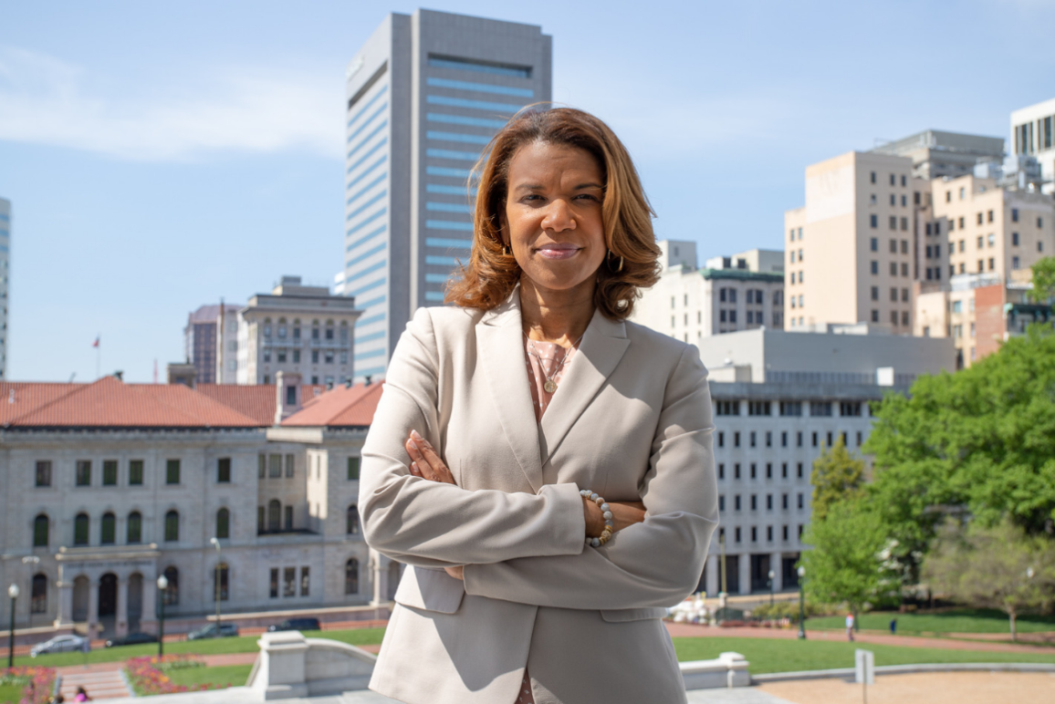 A picture of our Campaign Director Kemba Smith Pradia, a confident, strong-willed black woman standing with her arms folded in front of her chest, with buildings and courthouses in the background.