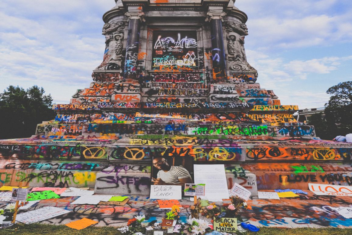 A photo of the base of the Lee statue, with graffiti all over and a memorial to Marcus-David Peters