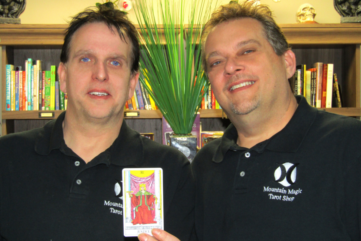 Picture of our client Mark Mullins and his husband, Jerome, holding a Tarot card that says "Justice"