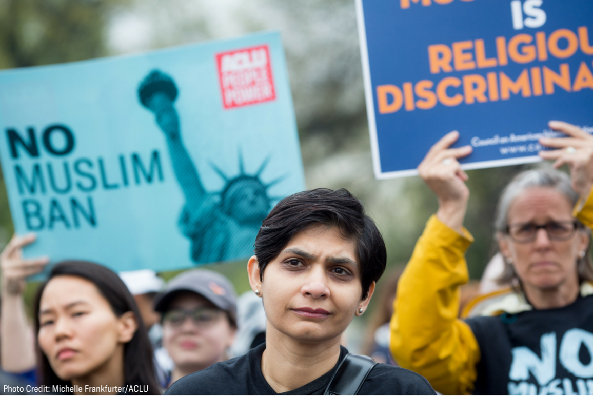 Photo of a protest against the Muslim Ban, with a Muslim woman in the foreground and an ACLU poster that said "No Muslim Ban" in the background