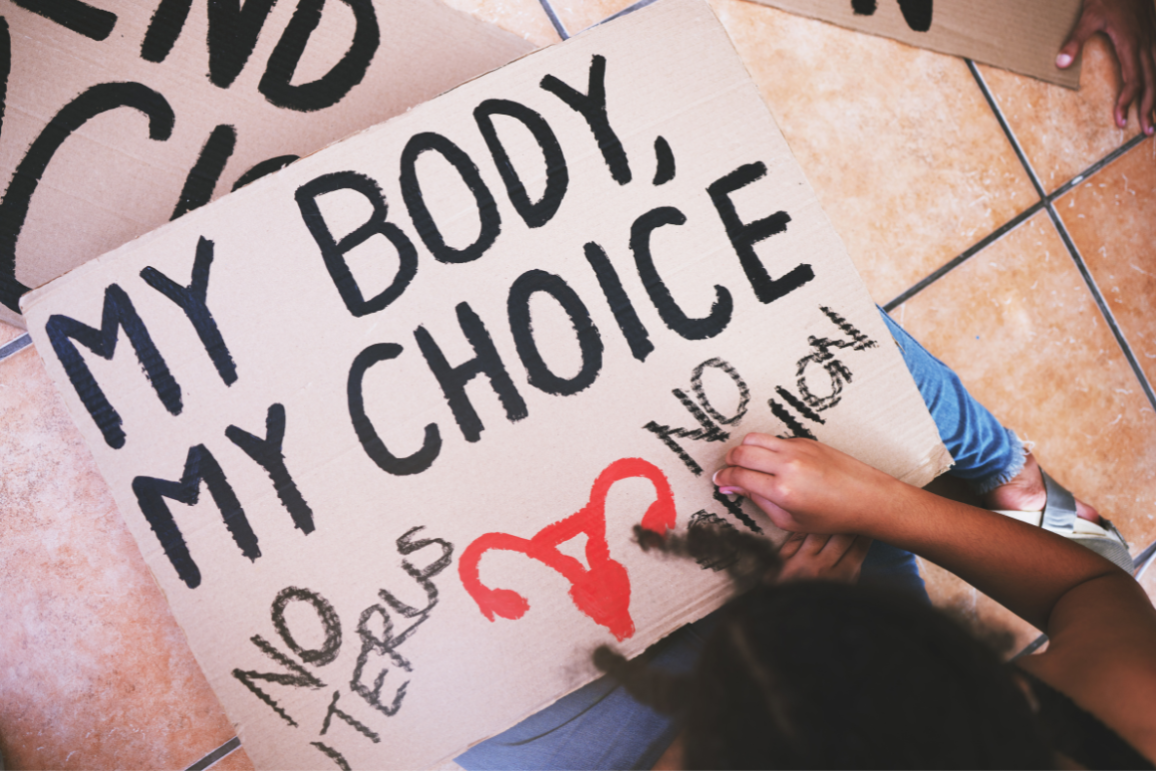 A protester in the process of writing on their sign, which reads "my body, my choice, no uterus, no opinion."