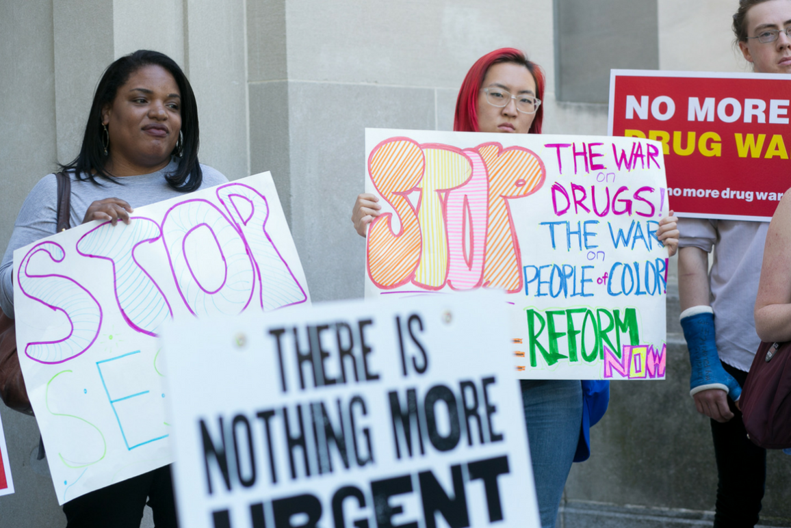 Protesters holding signs that say Stop The War on Drugs, the war on people of color, reform now.