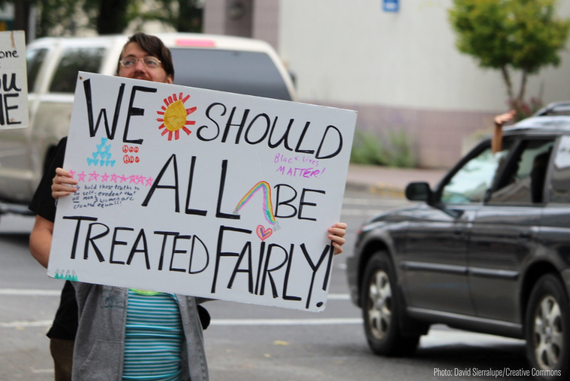 a protester holding a sign that says "We should All be Treated Fairly"