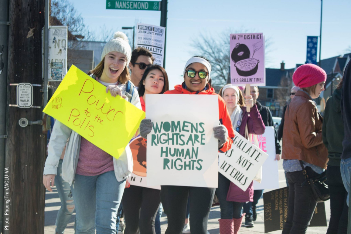 picture from the 2018 Women's March in Richmond, of a dark-skinned woman holding a sign that said "women's rights are human rights" and another white woman holding a sign that said "Power to the Polls"