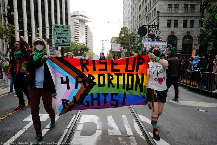 People holding a rainbow flag banner reading "Rise Up 4 Abortion Rights" while marching at the 2022 San Francisco Pride parade of 2022.