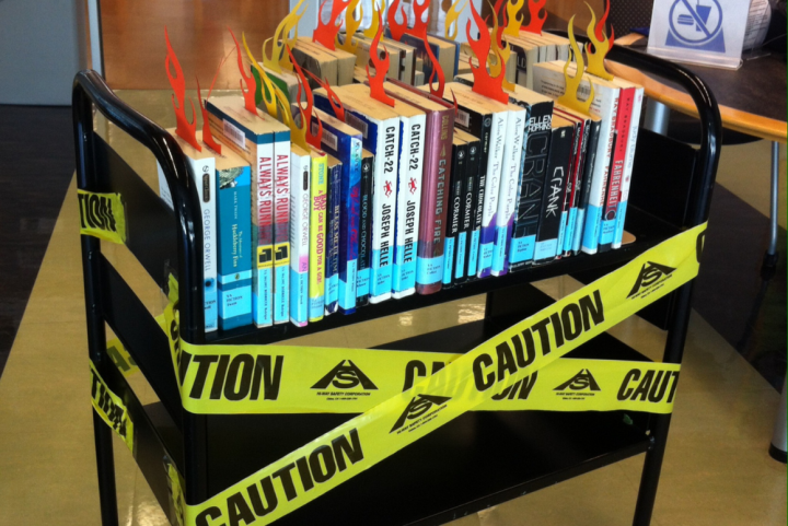 a Black book shelf with a few banned titles and the yellow tape that says "Caution"