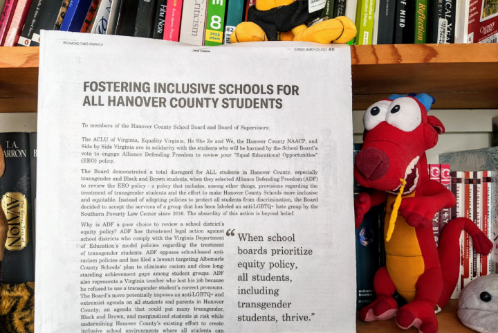 photo of a full-page newspaper opinion ad titled "Fostering inclusive schools for all Hanover County students," with a bookshelf in the background and a stuffed animal (Mushu the red dragon from Disney's Mulan) to the right of the newspapers. 