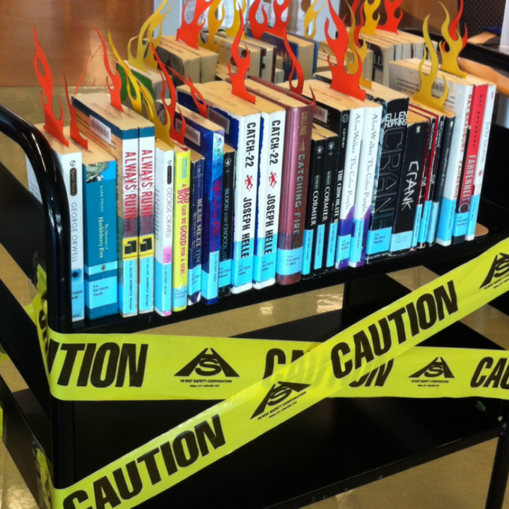 a Black book shelf with a few banned titles and the yellow tape that says "Caution"