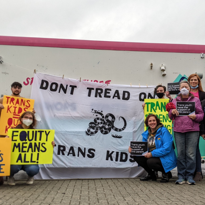 a group of parents and community advocates standing in front of Studio Two Three truck with a banner in the center that reads "Don't Tread on Trans Kids". Community members held pro-trans rights signs like "Let students thrive" and "Trans kids are our kid