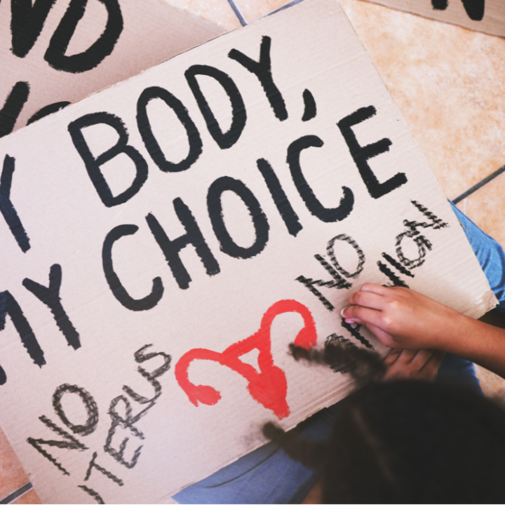 A protester in the process of writing on their sign, which reads "my body, my choice, no uterus, no opinion."